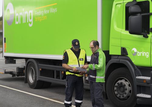 En medarbetare från tull kollar igenom papper från en Bring chaufför som står bredvid en Bring lastbil.