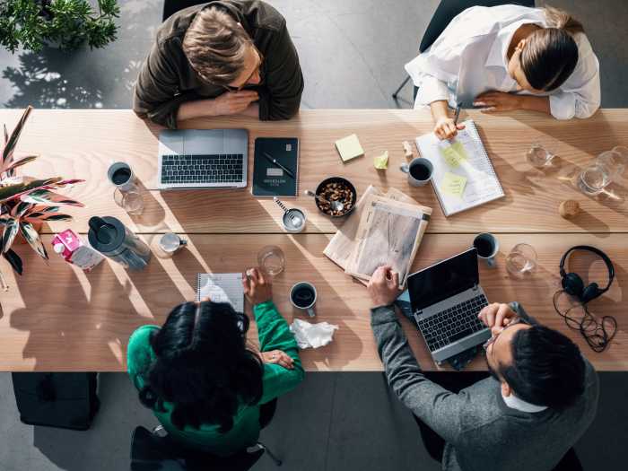 Fyra människor sitter vid ett bord, med laptops, kaffekoppar och anteckningsblock