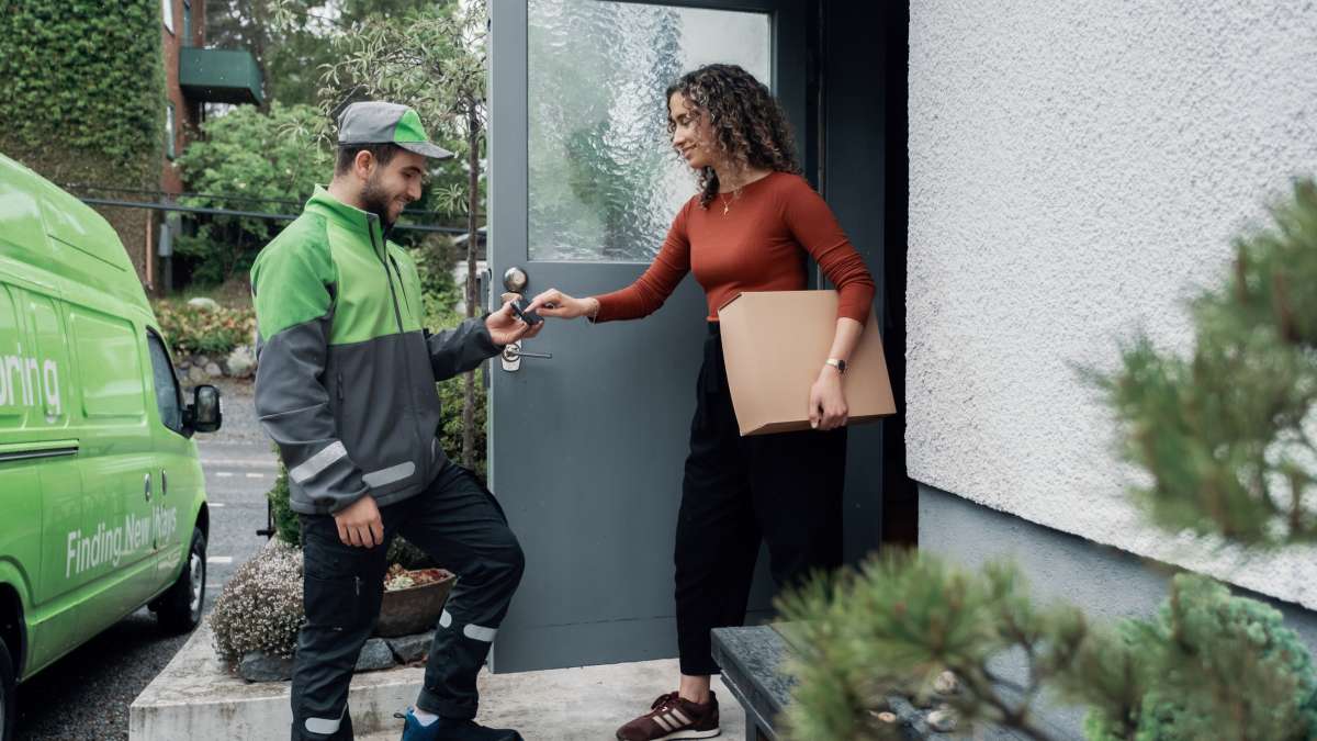 Ett Bringbud levererar ett paket till dörren hos en kvinna som signerar för leveransen på en telefon