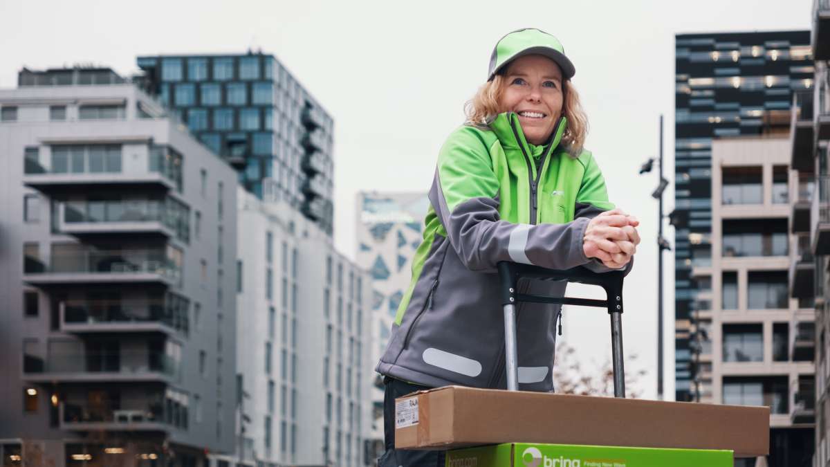 En kvinnlig medarbetare från Bring står lutad över en palldragare med paket på i stadsmiljö