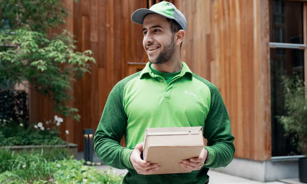 A Bring driver stands holding a parcel in front of him.