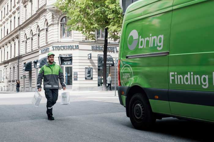 Ett Bringbud går med två påsar i händerna mot en Bring budbil från en butik