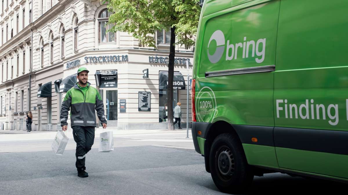 Ett Bringbud går med två påsar i händerna mot en Bring budbil från en butik