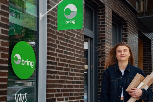 Tjej med paket i famnen, utanför ett Bring paketombud.